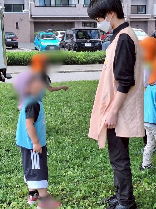 保育士を目指す専門学生の男の子と、保育園に通う園児が草むらで見つめ合っている様子