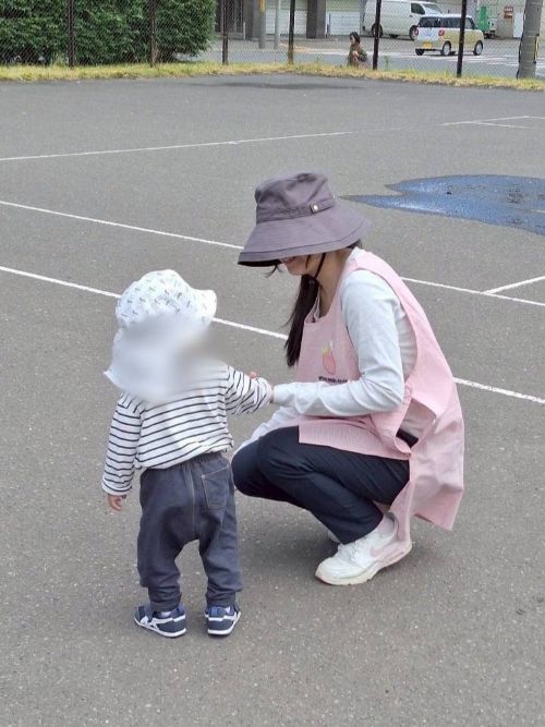 保育士を目指す専門学生の女の子と、保育園に通っている小さな園児が、アスファルトの上で手をつないで微笑んでいる様子
